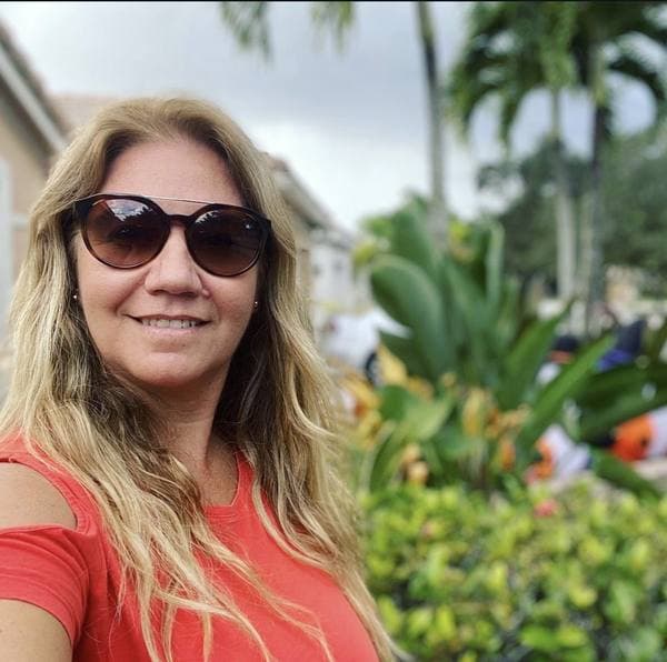Maria Iraola sonriendo al aire libre, con lentes de sol y plantas tropicales detrás