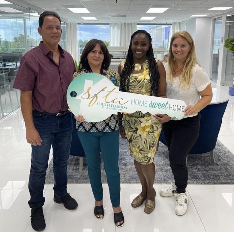 Maria Iraola and three smiling people in a bright office, holding a giant key sign that reads Home Sweet Home