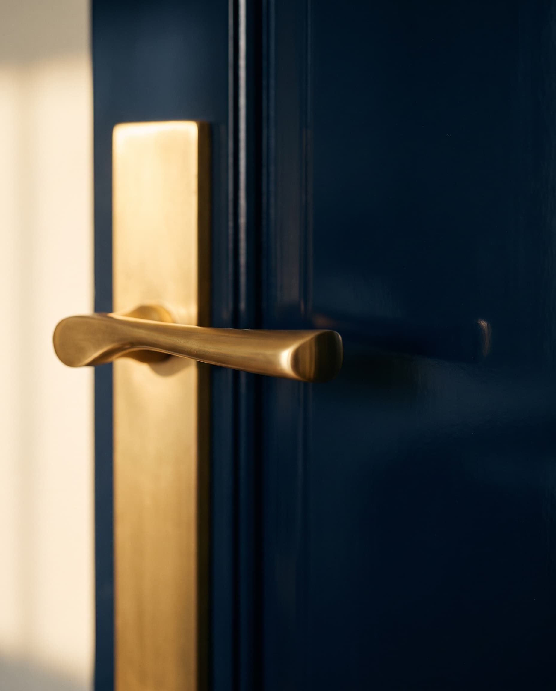 A brass lever on a glossy navy door, in warm afternoon light